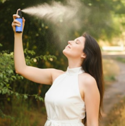 Mujer con ojos cerrados recibiendo una bruma de spray de herbolaria en el rostro rodeada de un entorno natural y verde
